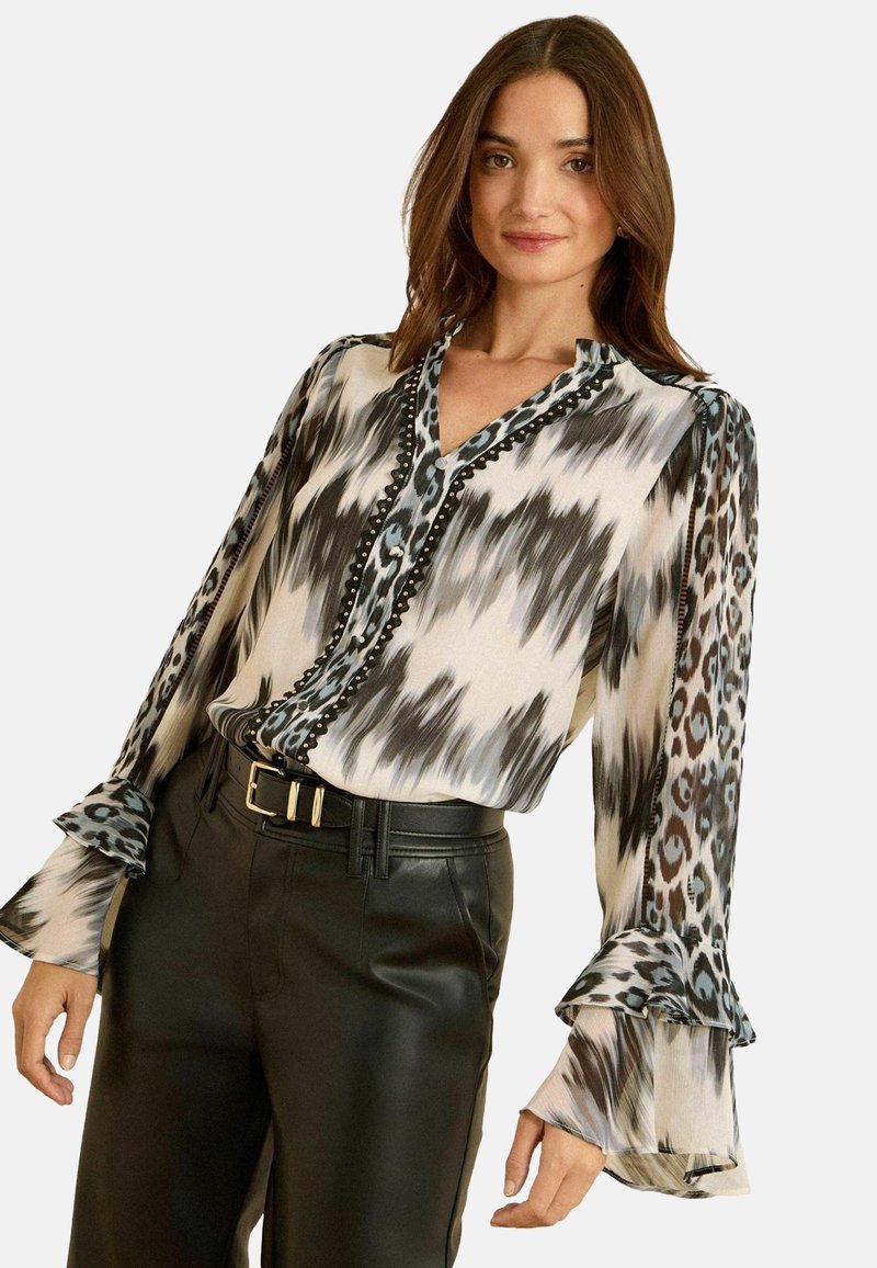 Hosszú ujjú blúz könnyű anyagból, fekete-fehér ikat mintával, állatmintás részletekkel és fodros mandzsettákkal. Fekete nadrág tartozék.