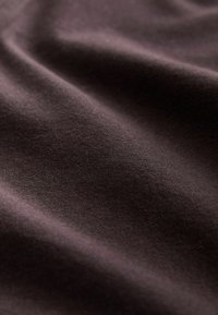 Surface en tissu brun foncé, douce et lisse, avec de légers plis et un éclairage subtil créant des ombres et des détails de texture.