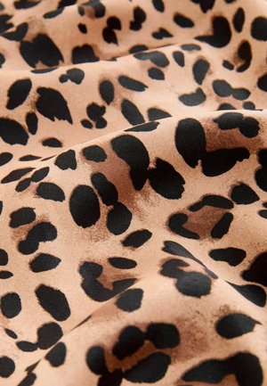 Tissu à motif léopard avec un fond beige clair, parsemé de taches noires de tailles et de formes variées, texture douce et finition lisse.