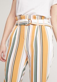 Pantaloni a righe con una vita alta, caratterizzati da strisce verticali gialle, verdi e rosa, e una cintura con una fibbia metallica tonda.