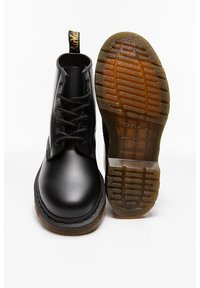 Botas de tobillo negras de cuero con puntera redonda, diseño de cordones y tirador amarillo. Suela de goma con agarre texturizado. Acabado suave y estilo clásico.