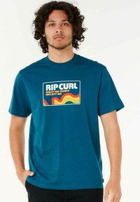 Teal kortærmet t-shirt lavet af bomuld, med et flerfarvet retro-grafik med "RIP CURL" tekst og bølgede accenter på forsiden.