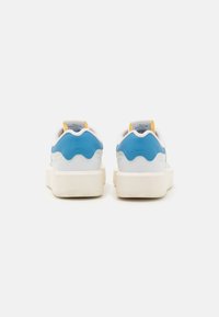 Białe sneakersy z niebieskimi i żółtymi akcentami, posiadające gładką skórzaną cholewkę, teksturowane fale po boku oraz grubą, teksturowaną podeszwę.