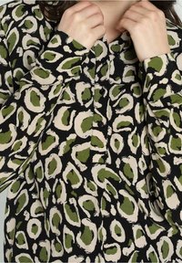 Camicia button-up nera con una stampa astratta di leopardo verde e beige. Presenta un colletto e maniche lunghe, in tessuto testurizzato.
