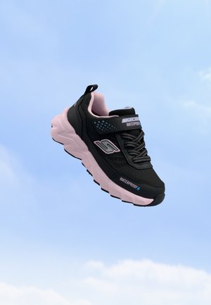 Baskets imperméables Skechers noires et roses flottant devant un ciel bleu clair.