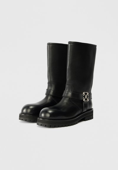 Μαύρες δερμάτινες μπότες μέχρι το γόνατο με στρογγυλή μύτη, φαρδύ άνοιγμα και διακοσμητική ασημένια μεταλλική λεπτομέρεια στο πλάι. Υφασμάτινη σόλα.