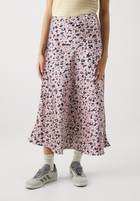 Rosa midi-skjørt med svart og hvit blomstermønster, glatt tekstur, utsvulmet design, brukt sammen med grå joggesko og beige sokker.