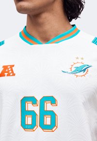 Άνδρας που φοράει λευκή φανέλα Miami Dolphins με αριθμό 66, τιρκουάζ και πορτοκαλί περιθώριο και λογότυπο AFC στο στήθος.