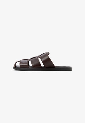 Brown leather slide sandal with a wide strap design, open-toe style, and a flat black sole. Features a smooth texture and minimal detailing.