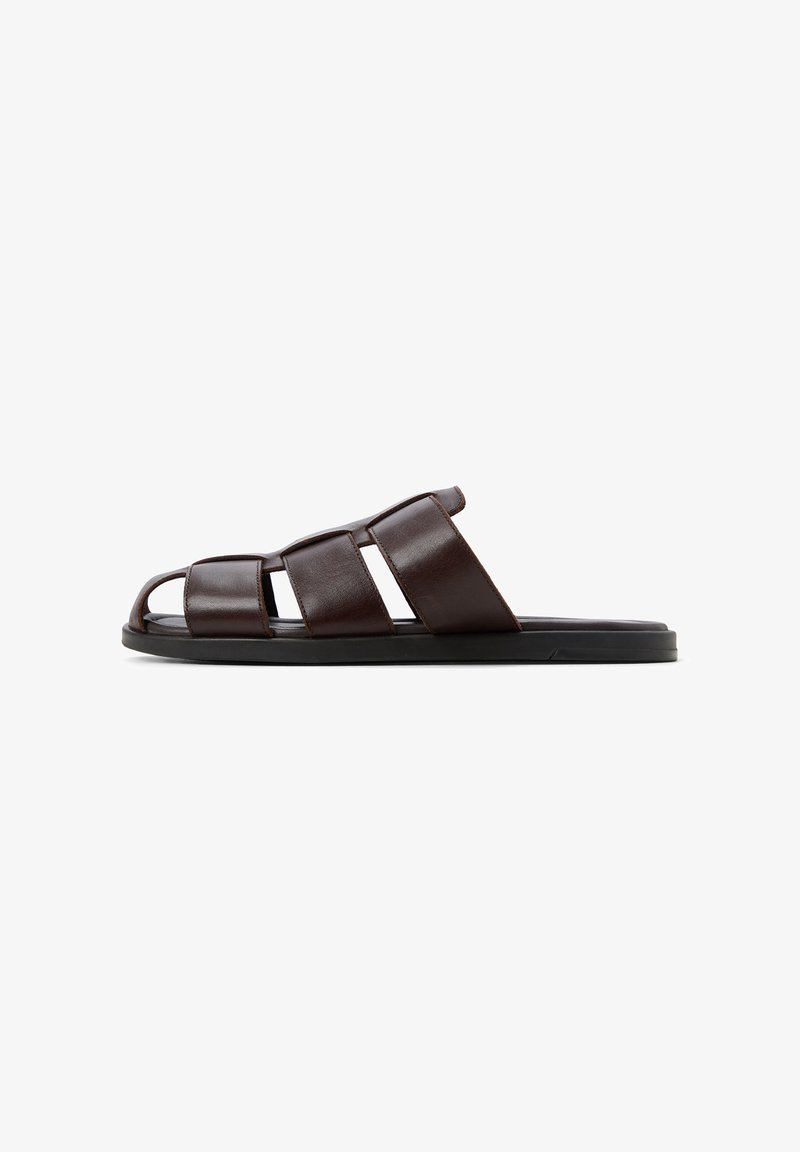 Braune Leder-Sandale mit breitem Riemen-Design, offener Zehenstil und flacher schwarzer Sohle. Besitzt eine glatte Textur und minimale Details.