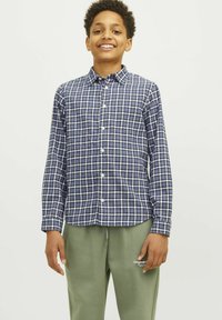 Cămașă în carouri albastre și albe cu guler butonat și mâneci lungi, fabricată dintr-un material moale. Purtați cu pantaloni de trening verzi cu un logo.