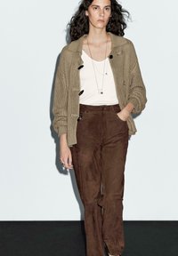 Beige stickad cardigan med stora svarta knappar, vit t-shirt och bruna mockabyxor. Enkel silversmycken fulländar outfiten.
