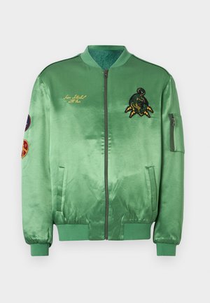 Groene satijnen bomberjack met geborduurde patches, voorzien van een rits vooraan, geribbelde manchetten en tailleband. Decoratieve stiksels aan de voorkant.