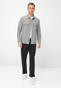 Grauhemd mit Knopfleiste und zwei Brusttaschen, kombiniert mit schwarzen Hosen und weißen Sneakers. Der Stoff wirkt glatt und leicht, mit einer taillierten Passform.
