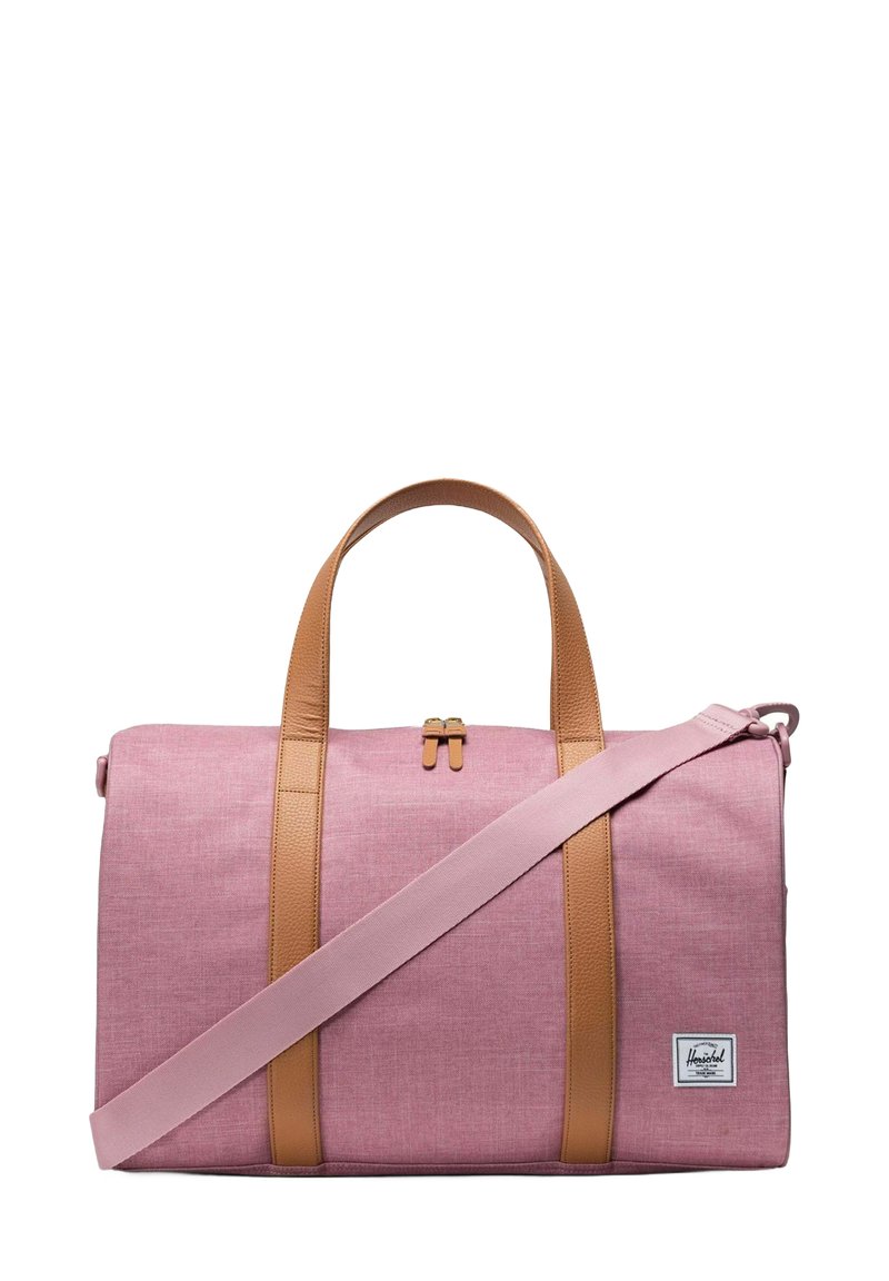 Sac de voyage en textile rose avec des poignées et une sangle en cuir marron. Comprend une fermeture éclair et une étiquette avec le logo Herschel sur le côté. Texture lisse.