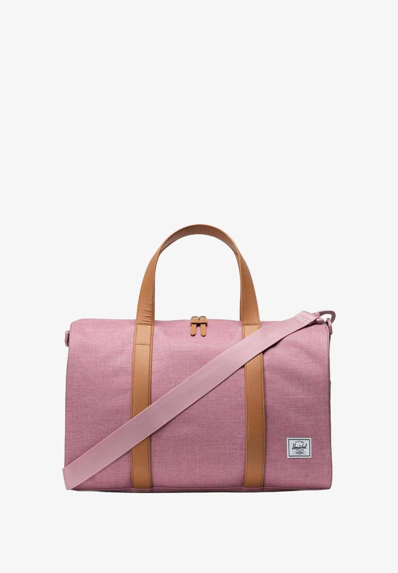 Sac de voyage en textile rose avec des poignées et une sangle en cuir marron. Comprend une fermeture éclair et une étiquette avec le logo Herschel sur le côté. Texture lisse.