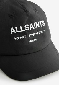 Svart keps i texturerad tyg med broderad vit "ALLSAINTS"-text, japanska tecken och "LONDON"-detalj på framsidan.
