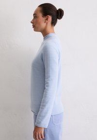 Hellblauer Pullover mit langen Ärmeln, hohem Kragen, weicher Textur und figurbetontem Design. Mit gerippten Bündchen und Saum für zusätzliche Details.
