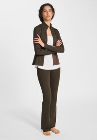 Brun idrottsjacka med hög krage, tillsammans med en vit topp och bruna vida byxor; slät tyg med en figurnära design.