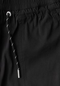 Shorts noirs avec une taille à cordon de serrage et des coutures blanches. Texture lisse avec des coutures visibles et un accent métallique à l'extrémité du cordon.