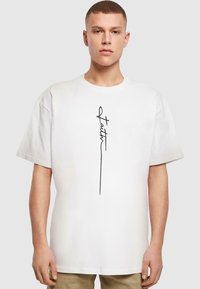 Hvid bomulds T-shirt med et lodret sort håndskrevet tekstdesign. Rund halsudskæring og løs pasform med korte ærmer.