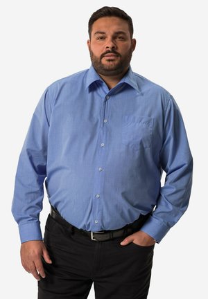 Camisa de botón de manga larga azul claro con un bolsillo en el pecho, tela texturizada y cuello. Combinada con pantalones negros y un cinturón.