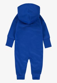 Modrý overal s kapucňou z mäkkého materiálu, s dlhými rukávmi, okrúhlym výstrihom, rebrovanými manžetami a patentkami na spodnej časti.