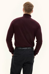 Bordeauxroter Rollkragenpullover mit geripptem Kragen, kombiniert mit schwarzer Hose mit Gesäßtaschen. Glatte Textur mit tailliertem Schnitt.