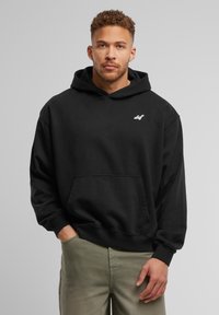 Hoodie noir avec une poche kangourou à l'avant, des poignets côtelés et un logo blanc sur la poitrine. Matière douce avec une coupe décontractée.