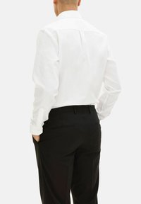 Witte blouse met lange mouwen, een klassieke kraag, knopenmanchetten en een rechte rugnaad, gecombineerd met zwarte broek.