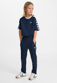 Marineblauwe sportset bestaande uit een t-shirt met witte accenten en een logo, gecombineerd met bijpassende joggers met zijzakken en strepen.