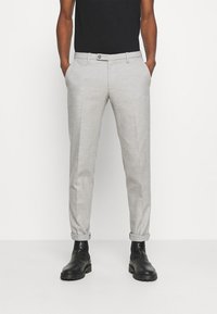 Pantalon gris clair en tissu tissé, coupe slim, avec des poches avant, des ourlets retournés et une fermeture à bouton unique. Associé à des bottes noires.