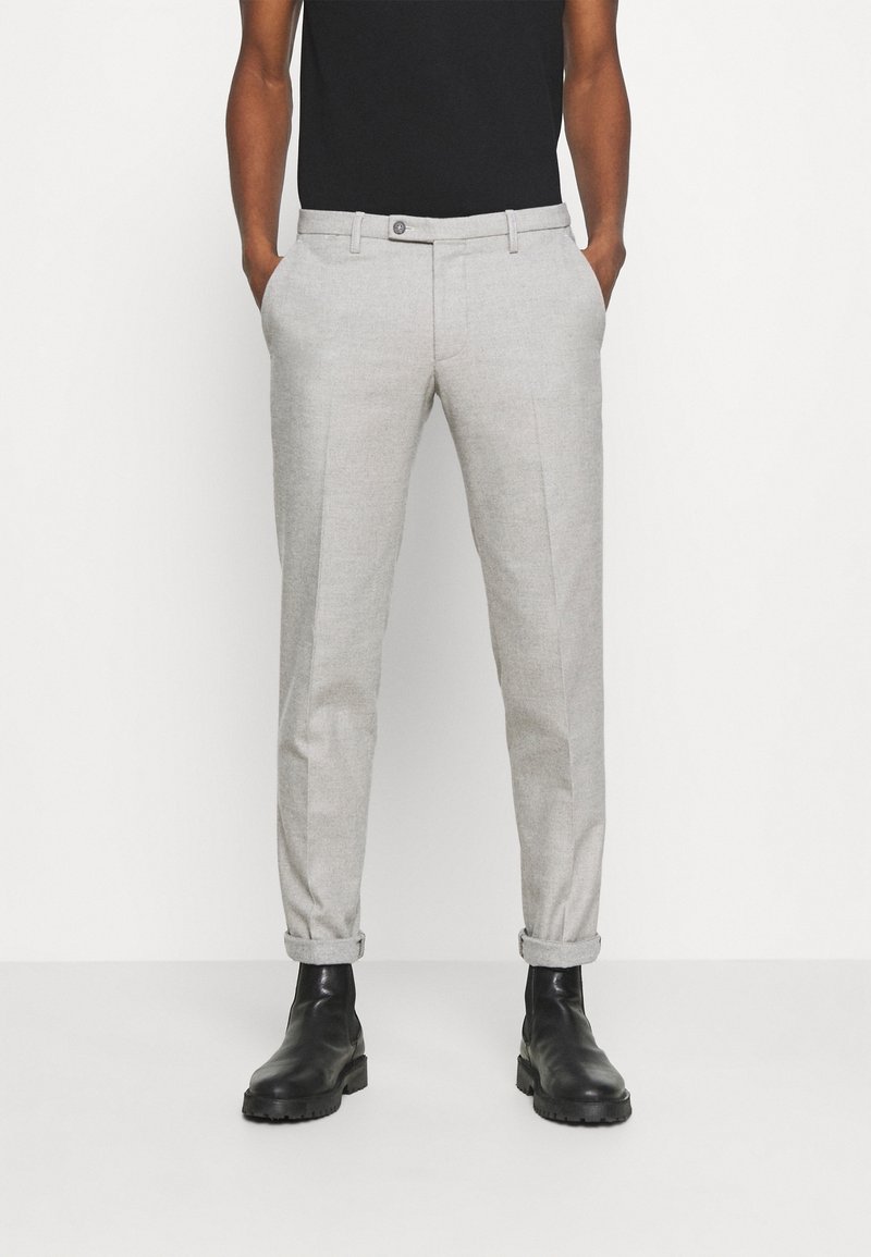 Pantalon gris clair en tissu tissé, coupe slim, avec des poches avant, des ourlets retournés et une fermeture à bouton unique. Associé à des bottes noires.