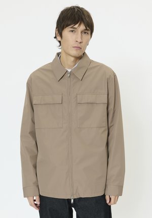 Veste légère marron avec une fermeture éclair à l'avant, deux poches poitrine et un col. Texture lisse avec des manches longues, conçue pour une coupe décontractée.