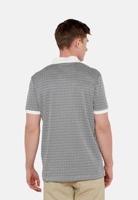 Camisa polo de manga corta con un patrón de diamantes en blanco y negro, con un cuello y acentos de puño blancos, mostrada desde la parte de atrás.
