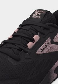 Κοντινή λήψη μαύρου και ροζ αθλητικού παπουτσιού Reebok με διχτυωτό ύφασμα, κορδόνια και λεπτομέρειες με το λογότυπο στη γλώσσα και στην πλαϊνή πλευρά.