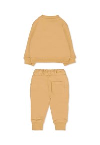 Completo sportivo in beige chiaro composto da una felpa con girocollo e pantaloni jogger coordinati, dotati di vita elastica e tasca laterale. Texture liscia.