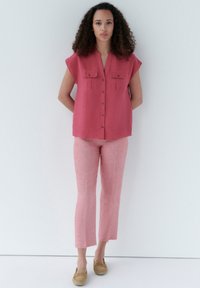 Roze overhem speler met korte mouwen en twee borstzakken, gecombineerd met lichtroze cropped broek. Gemaakt met tan instap schoenen.