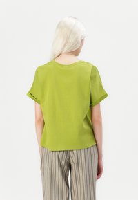 Short-sleeved, round-neck t-shirt in bright green cotton. Smooth texture with casual fit and rolled sleeve cuffs. Worn with striped pants.