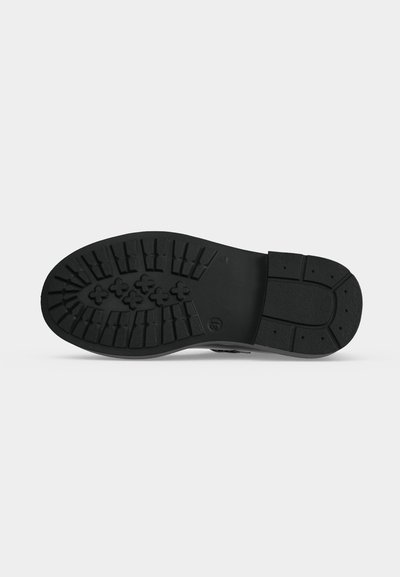 Semelle de chaussure noire avec des rainures profondes et des motifs en forme de croix sur la moitié avant, présentée sur un fond gris clair uni.