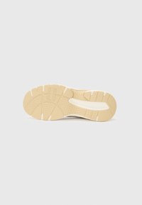 Sole of a sneaker in beige rubber, featuring a textured pattern with grooves and ridges for grip, and a white accent along the side.