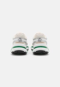 White and silver athletic shoes with mesh fabric, green accents, and black outsole. Features padded collar and heel support.