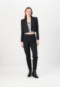 Zwarte cropped blazer met gestructureerde schouders over een denim bustier, gecombineerd met hoge zwarte jeans en zwarte haklaarzen.