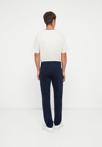 Light beige short-sleeve t-shirt with a navy collar, paired with dark navy slim-fit pants. The outfit features a clean, modern design.