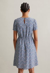 Kurzarmkleid aus blauer Stoff mit floralen Mustern, elastischem Bund und Schlüsselloch-Ausschnitt auf der Rückseite. Geschmeidige Textur.