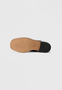 Semelle de chaussure noire avec un design perforé. Comprend une semelle intermédiaire lisse couleur tan et un talon noir texturé. Marquage visible près du talon.