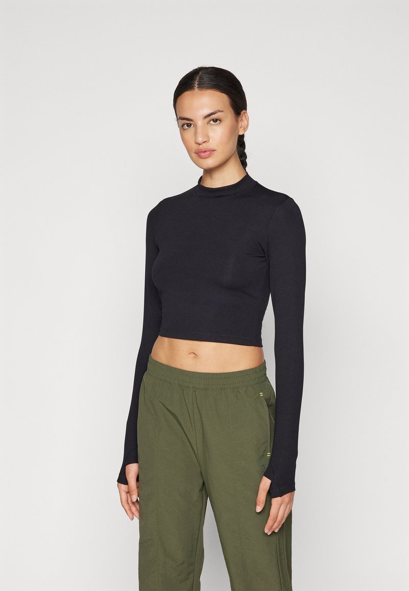 Black cropped long-sleeve top with a fitted design and high neckline, paired with loose olive green pants featuring elastic waistband.