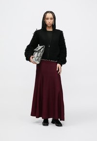 Černý žebrovaný svetr na zip s kožešinovými rukávy, vrstvený přes bordó rozšířenou sukni. Drží černo-bílou kabelku s hadím motivem.