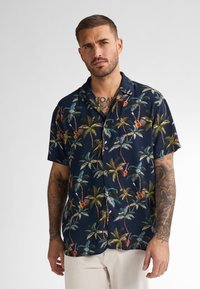 Camicia a maniche corte di colore blu navy con motivo tropicale di palme e chitarre. Realizzata in tessuto leggero con una vestibilità rilassata e chiusura a bottoni.