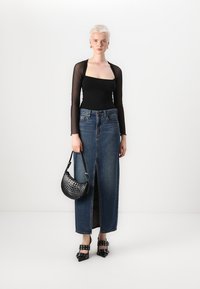 Schwarzes Langarmoberteil, hoch geschnittene Denim-Maxi-Rock mit Schlitz vorne, schwarze Tasche mit Nieten und schwarze Absatzschuhe mit Schnallen.